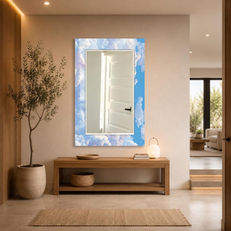 May include: A rectangular wall mirror featuring a decorative border printed with a bright blue sky and white fluffy clouds. The central reflective glass surface shows a clear reflection of a white interior door with a black handle.