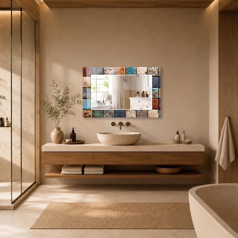 May include: A rectangular wall mirror featuring a decorative frame composed of small, multi-colored square tiles in shades of blue, brown, orange, and cream. The mirror has a reflective glass center that displays a view of a bathroom interior.