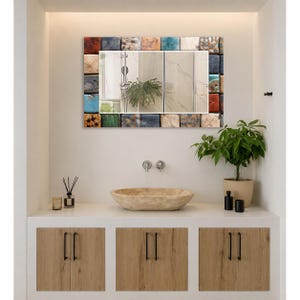 May include: A rectangular wall mirror featuring a decorative frame composed of small, multi-colored square tiles in shades of blue, orange, brown, and cream. The reflective surface shows a bathroom interior with a shower head and a green plant.