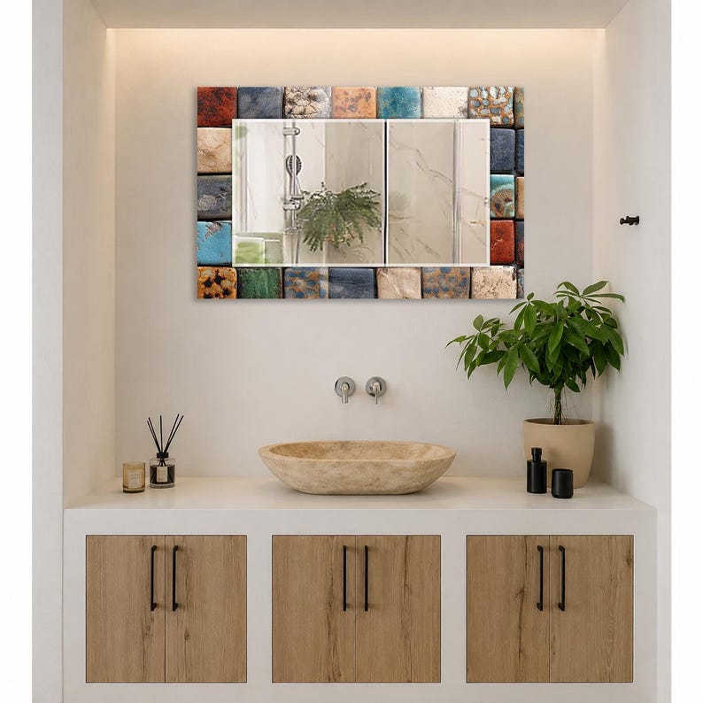 May include: A rectangular wall mirror featuring a decorative frame composed of small, multi-colored square tiles in shades of blue, orange, brown, and cream. The reflective surface shows a bathroom interior with a shower head and a green plant.