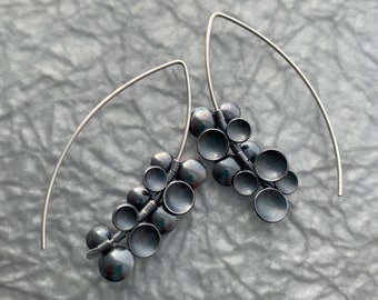 May include: A pair of silver earrings with a cluster of small, round, black beads hanging from each earring. The earrings are suspended from a thin, silver wire.