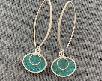May include: A pair of silver dangle earrings with turquoise oval-shaped stones. The stones have a white circle design inside.