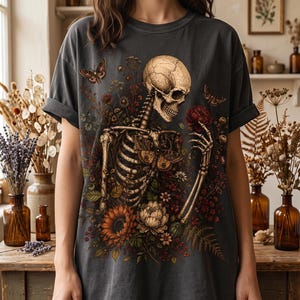 A person wearing a dark grey oversized T-shirt with a detailed illustration of a floral skeleton graphic on the front.