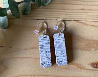 May include: A pair of silver earrings with white paper ticket charms. The tickets have black text and say "South J. Ave. - North J. Ave. - Angeles Park - Change of Trains - Nov. 4 - 11:14 A.M."