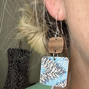 May include: A pair of dangle earrings with a square wooden top and a square bottom featuring a blue and white pattern of birds in flight.