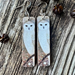 May include: A pair of owl earrings with a white owl on a brown background. The earrings are made of wood and have silver hooks.