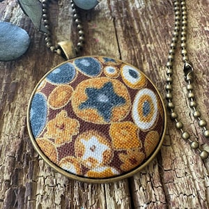 May include: A round pendant necklace with a brown, yellow, and blue floral pattern. The pendant is attached to a brass chain.