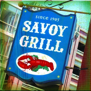 May include: A blue Savoy Grill sign with white text and a red lobster illustration. The sign reads "Since 1903" at the top. The sign is hanging outside a building.