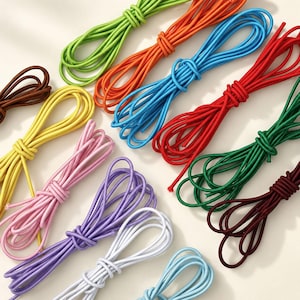 May include: A collection of twelve coiled elastic cords in various solid colours including lime green, orange, bright blue, red, dark green, brown, yellow, pink, purple, white, light blue, and maroon, each tied into a simple loop for organisation.
