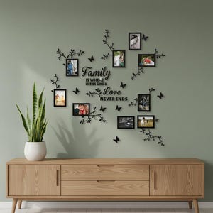May include: A black wall-mounted photo frame collage featuring eight rectangular frames arranged among decorative black metal branches and butterfly silhouettes. The centre text reads Family IS WHERE LIFE BE GINS & Love NEVER ENDS.