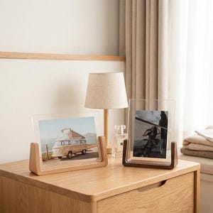 May include: Two rectangular clear acrylic photo frames with wooden bases. One frame is oriented horizontally, displaying a vintage van, and the other is oriented vertically, displaying a person. The bases are made of light and dark wood.
