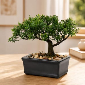 Op de afbeelding: Een kleine kunstmatige bonsaiboom met levendige groene bladeren en een getextureerde bruine stam, geplant in een rechthoekige zwarte keramische pot gevuld met gladde, veelkleurige decoratieve rivierstenen aan de basis.