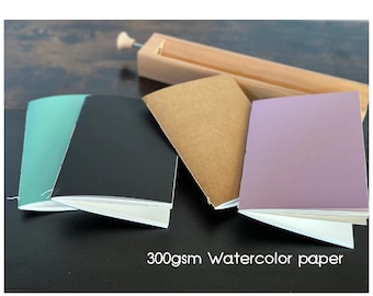 May include: Four small notebooks with different colored covers: teal, black, brown, and purple. The notebooks are made with 300gsm watercolor paper.