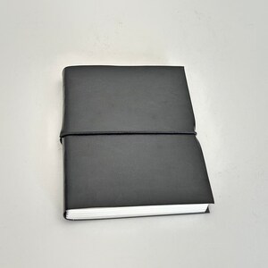 May include: A black leather-bound journal with a simple design and a black elastic band closure.