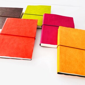 May include: Five small, colourful notebooks with elastic closures. The notebooks are brown, green, pink, orange, and red.