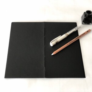 May include: A black sketchbook with a white pen and a brown pencil with the text "GENERAL'S CHARCOAL WHITE 308" on it.