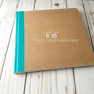 Puede incluir: Un cuaderno de bocetos marr&oacute;n con una encuadernaci&oacute;n turquesa. La portada tiene el texto "6" x "6" 300 g/m&sup2; papel mixto" impreso.
