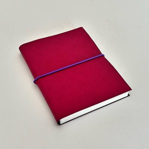 May include: A small, crimson red notebook with a purple elastic band wrapped around it.