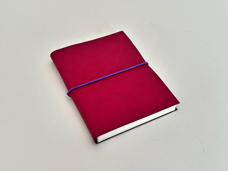 May include: A small, crimson red notebook with a purple elastic band wrapped around it.