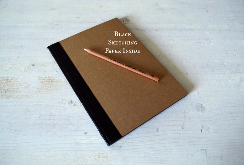 Pode incluir: Um caderno de desenho marrom com uma lombada preta e o texto "Black Sketching Paper Inside". Um l&aacute;pis est&aacute; em cima do caderno.