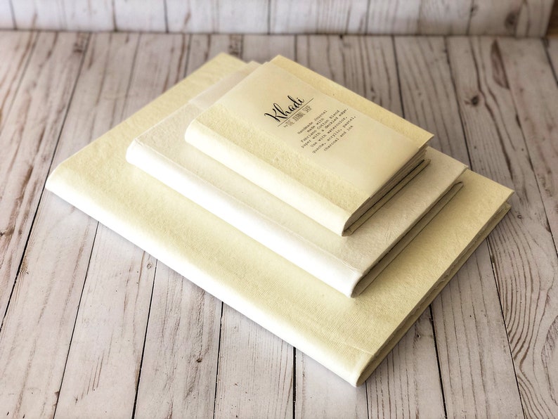 May include: Three cream-colored notebooks stacked on top of each other. The top notebook has the text "Khaki The Journal Joy" printed on the cover.