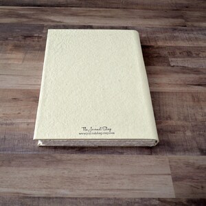 May include: A cream-colored journal with a textured cover and the text "The Journal Shop" and "www.thejournalshop.etsy.com" printed on the back.