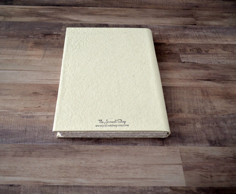 May include: A cream-colored journal with a textured cover and the text "The Journal Shop" and "www.thejournalshop.etsy.com" printed on the back.