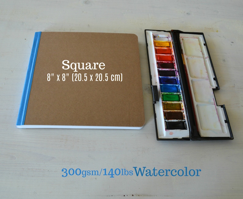 Puede incluir: Un cuaderno de bocetos cuadrado de acuarela marr&oacute;n con una encuadernaci&oacute;n azul. El cuaderno mide 8 pulgadas por 8 pulgadas (20,5 cm x 20,5 cm) y es de papel de acuarela de 300 g/m&sup2; / 140 lb.