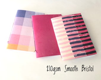 May include: Three notebooks with different patterned covers. The covers are pink, blue, and white with black stripes. The notebooks are made of 210gsm smooth Bristol paper.