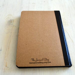 Pode incluir: A capa de tr&aacute;s de um di&aacute;rio marrom com uma lombada preta e o texto "The Journal Shop www.journalshop.etsy.com" impresso nela.