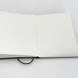 May include: A black blank notebook with a black elastic closure, open to reveal blank white pages.