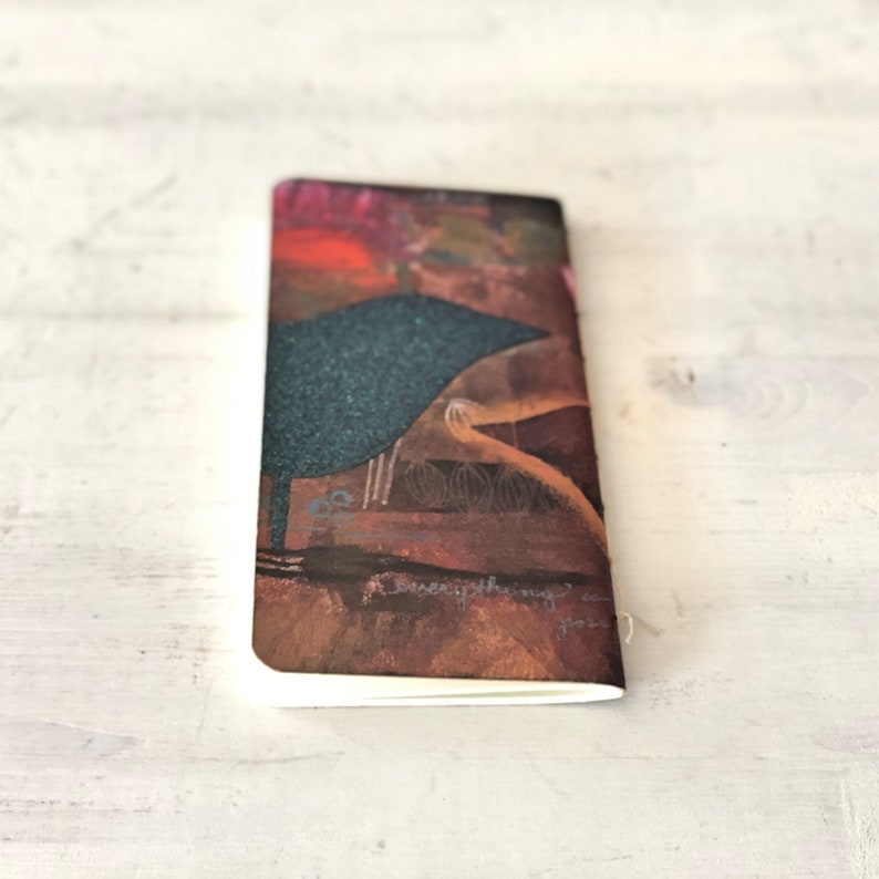 May include: A small, brown notebook with a colorful abstract design on the cover. The design features a dark blue shape, a light brown shape, and a red and orange shape. The text "everything is possible" is written on the cover.
