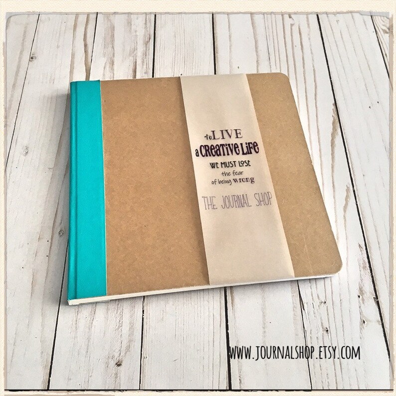 Puede incluir: Un diario marr&oacute;n con una encuadernaci&oacute;n turquesa y una etiqueta blanca con el texto "To LIVE a Creative LiFe WE MUST LOSE the fear of being WRONG THE JOURNAL SHOP" y la direcci&oacute;n del sitio web "WWW.JOURNALSHOP.ETSY.COM".