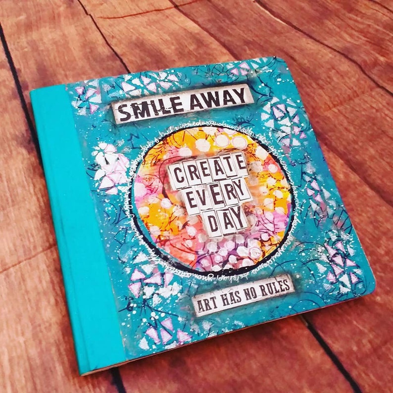Puede incluir: Una libreta turquesa con un dise&ntilde;o colorido y el texto "Smile Away" y "Create Every Day" en la portada. El texto "Art Has No Rules" tambi&eacute;n est&aacute; en la portada.