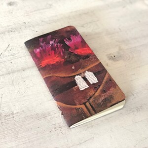 May include: A small, brown notebook with a colorful abstract design on the cover. The design features pink and red coral-like shapes and white paper scraps.