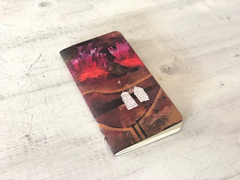 May include: A small, brown notebook with a colorful abstract design on the cover. The design features pink and red coral-like shapes and white paper scraps.