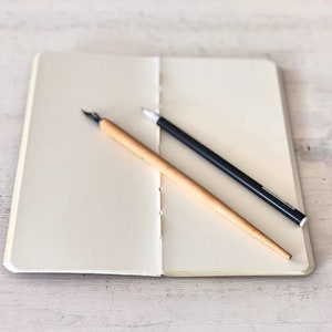 May include: A blank notebook with a black pen and a wooden calligraphy pen lying on top of it.