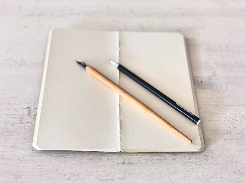 May include: A blank notebook with a black pen and a wooden calligraphy pen lying on top of it.