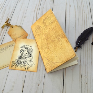 Pode incluir: Um diário de estilo vintage com um design de mapa dourado na capa. O diário está aberto para revelar páginas em branco. Também são mostradas uma pena e um tinteiro, juntamente com um cartão postal vintage e uma etiqueta.