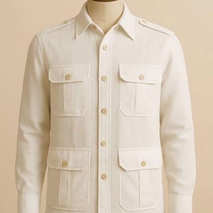 Pode incluir: Uma camisa utilitária de manga comprida em branco sujo, com colarinho clássico, presilhas nos ombros e quatro bolsos frontais com abas abotoadas. A camisa apresenta uma carcela central com botões a condizer em todo o seu design.
