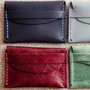 May include: Four rectangular card holders arranged in a grid. The top left is dark blue with light blue stitching, the top right is light gray with purple stitching, the bottom left is textured burgundy with pink stitching, and the bottom right is textured green with light green stitching.