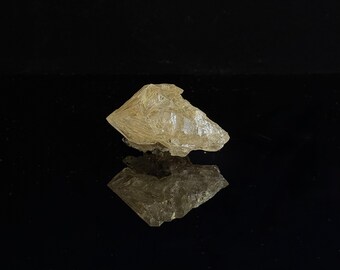 May include: A translucent, pale golden-yellow mineral specimen with a jagged, crystalline structure. The object features sharp, angular facets and a fibrous, needle-like internal texture, reflecting light across its irregular, multi-pointed surface.