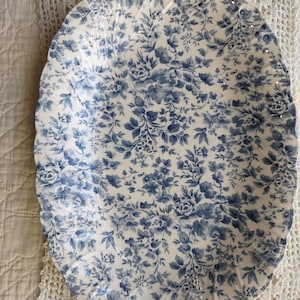 May include: An oval-shaped ceramic serving platter featuring a scalloped edge and a detailed blue floral pattern on a white background. The intricate design covers the entire surface of the dish, showcasing various leaves and small blossoms.