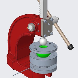 Puede incluir: Una prensa de husillo industrial roja con un mecanismo de cremallera vertical y un mango plateado. La máquina incluye un componente esférico blanco central posicionado sobre una pila de placas circulares grises y un inserto verde brillante.