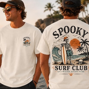Könnte beinhalten: Cremefarbenes T-Shirt mit einer kleinen Grafik auf der Vorderseite und einer großen Grafik auf der Rückseite, die ein Skelett mit Kappe und Shorts zeigt, das mit einem Surfbrett an einem Strand mit Palmen, Sonnenuntergang und dem Text Spooky Surf Club Saltwater After Dark steht.