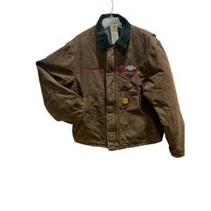 May include: A brown canvas work jacket featuring a dark green corduroy collar, a front zipper closure, and two lower pockets. The chest displays an embroidered logo with the text Vermont Transportation Agency. A small yellow brand tag is on the pocket.