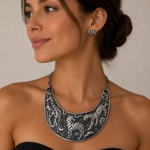 May include: A silver-toned crescent-shaped statement necklace featuring embossed wildlife figures including a giraffe, zebra, and leopard against a dark textured background, paired with matching small square stud earrings with black and white stripes.