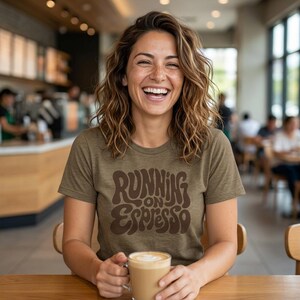 May include: A short-sleeved olive green t-shirt featuring the dark brown text Running on Espresso in a wavy, retro-inspired font. The shirt has a crew neckline and a standard fit, made from a textured fabric that appears soft and lightweight.