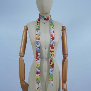 May include: A mannequin wearing a long, colorful scarf with a floral pattern. The scarf is tied around the mannequin's neck and hangs down to the mannequin's waist.