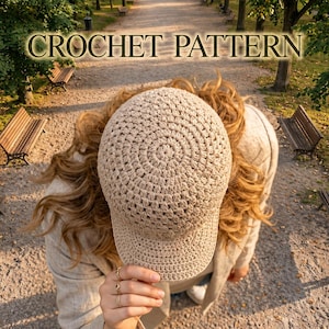 May include: A beige crochet baseball cap with a textured, circular stitch pattern on the crown and a firm brim. The text CROCHET PATTERN is displayed in a light font at the top of the image, centred above the hat.